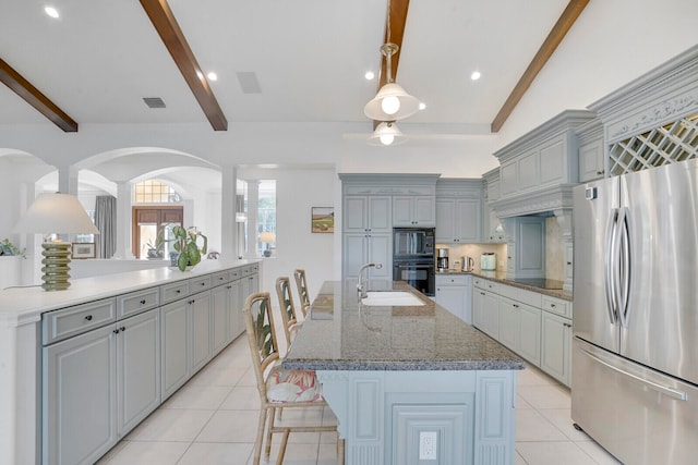 kitchen featuring stainless steel fridge, a kitchen breakfast bar, sink, gray cabinets, and an island with sink