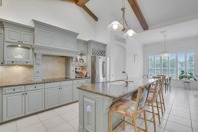 kitchen with stainless steel fridge, beam ceiling, a kitchen island with sink, and sink