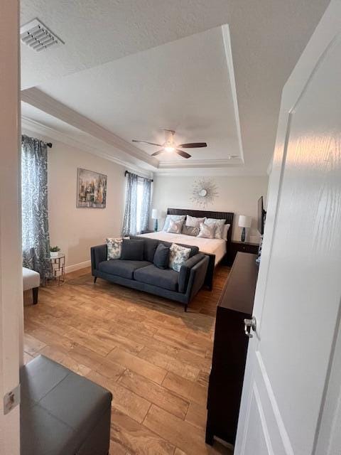 bedroom with light wood-type flooring, ceiling fan, and a raised ceiling