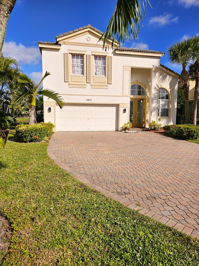 mediterranean / spanish home with a tile roof, an attached garage, decorative driveway, french doors, and stucco siding