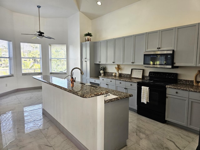 kitchen with black / electric stove, stainless steel microwave, marble finish floor, and dark stone countertops