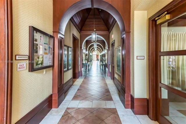 corridor featuring a chandelier, light tile patterned floors, arched walkways, and wallpapered walls