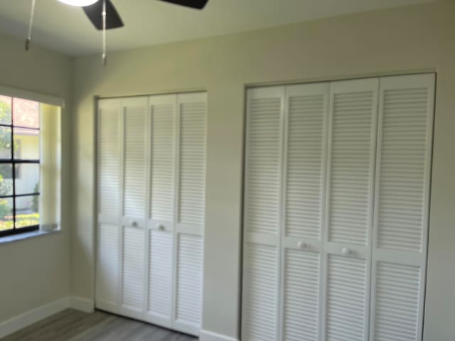 unfurnished bedroom with multiple closets, ceiling fan, and wood-type flooring