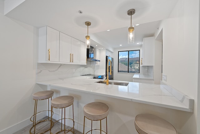 kitchen with white cabinets, decorative backsplash, wall chimney exhaust hood, kitchen peninsula, and light stone counters