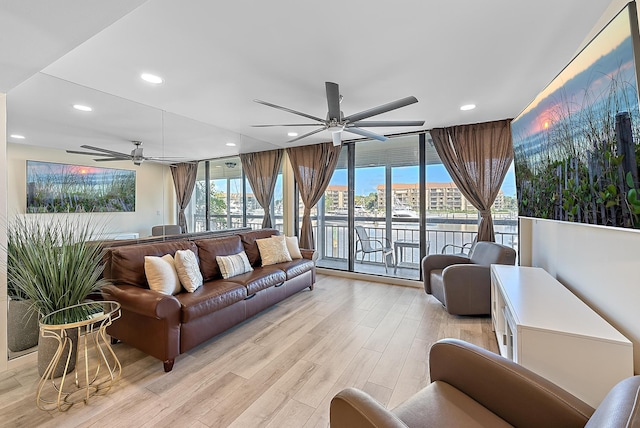 living room with a wall of windows, ceiling fan, and light wood-type flooring