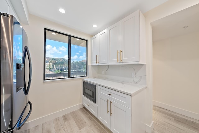 kitchen featuring black microwave, white cabinetry, light stone countertops, light hardwood / wood-style flooring, and stainless steel refrigerator with ice dispenser