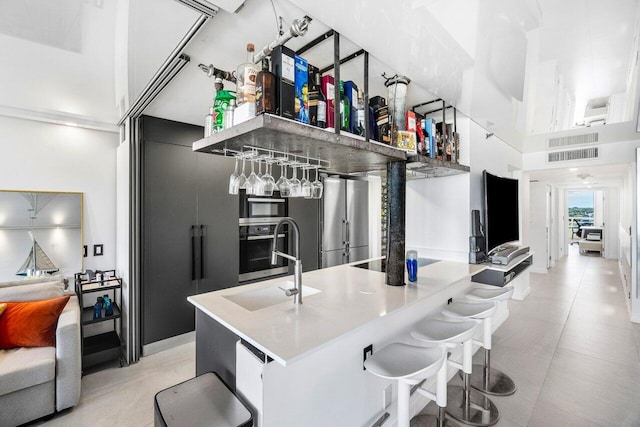 kitchen with sink, a kitchen island with sink, stainless steel appliances, and a high ceiling