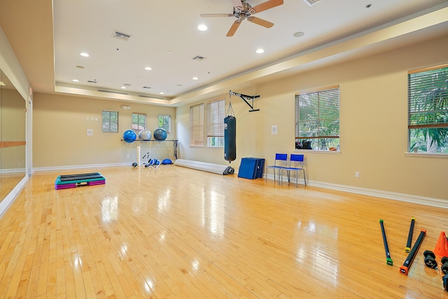 exercise area with ceiling fan, light hardwood / wood-style floors, and a raised ceiling