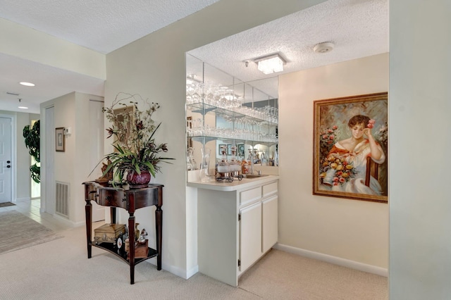 bar with white cabinetry, light carpet, and a textured ceiling