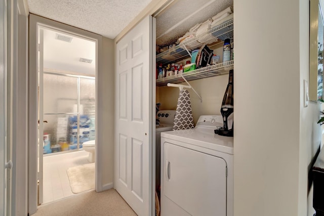 clothes washing area featuring washing machine and clothes dryer, light carpet, and a textured ceiling