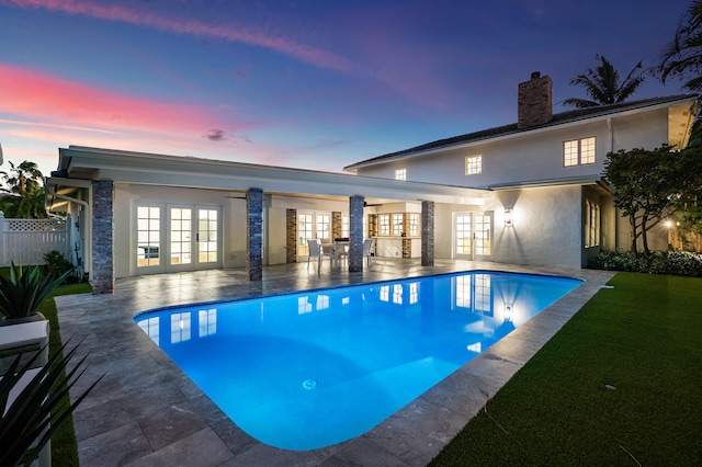 pool at dusk with a patio and french doors