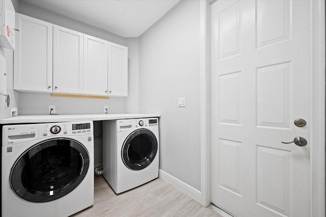 laundry room featuring washer and clothes dryer, light hardwood / wood-style floors, and cabinets