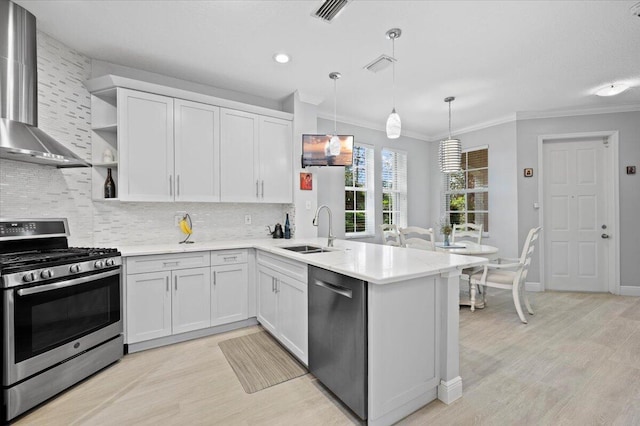 kitchen featuring appliances with stainless steel finishes, sink, wall chimney range hood, white cabinetry, and hanging light fixtures