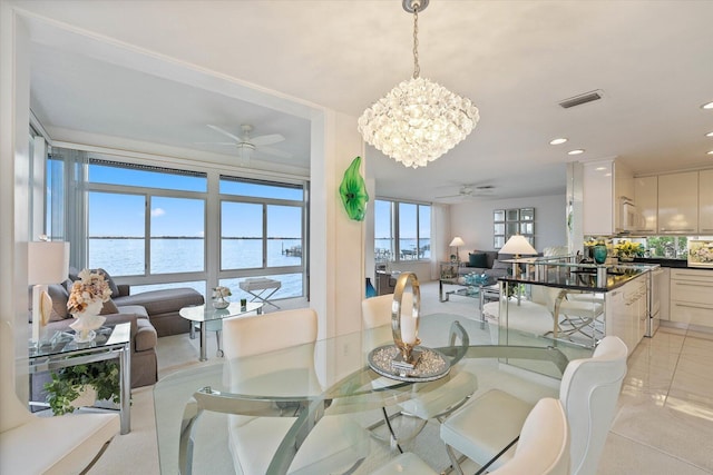 dining area featuring plenty of natural light, light tile patterned flooring, a water view, and ceiling fan with notable chandelier