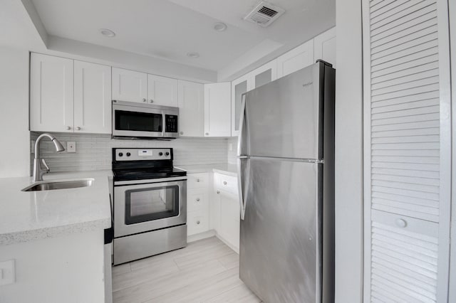 kitchen featuring light stone countertops, sink, decorative backsplash, white cabinets, and appliances with stainless steel finishes