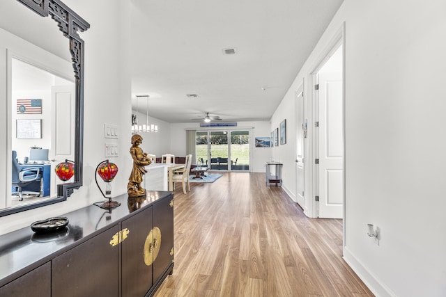 hallway with light hardwood / wood-style flooring and a notable chandelier