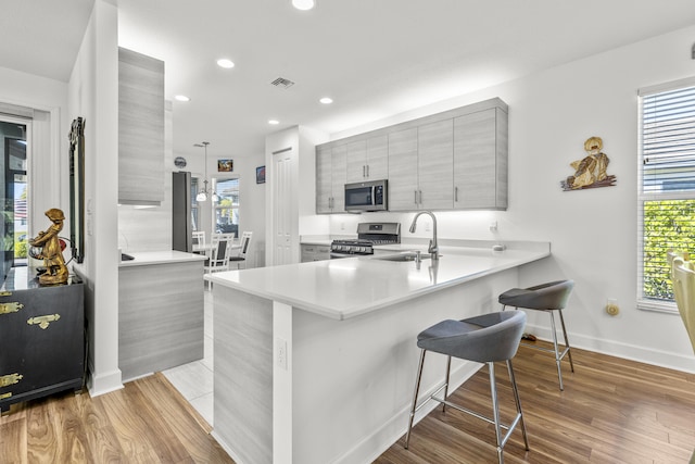 kitchen featuring gray cabinets, kitchen peninsula, stainless steel appliances, and light hardwood / wood-style flooring