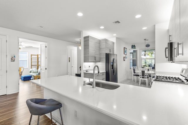 kitchen with kitchen peninsula, appliances with stainless steel finishes, a kitchen bar, sink, and light hardwood / wood-style floors