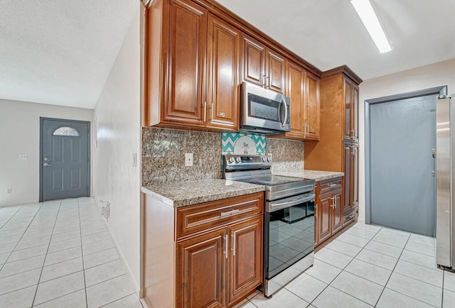 kitchen featuring backsplash, stainless steel appliances, light stone counters, and light tile patterned flooring