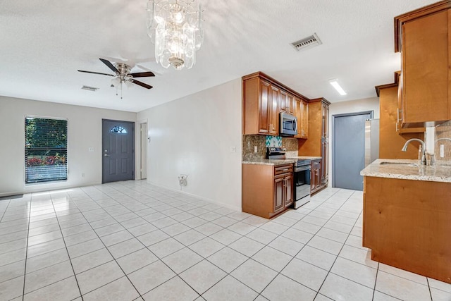 kitchen with appliances with stainless steel finishes, ceiling fan with notable chandelier, light stone counters, and sink