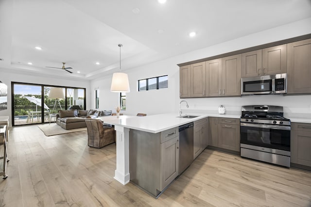 kitchen featuring kitchen peninsula, stainless steel appliances, a tray ceiling, decorative light fixtures, and light hardwood / wood-style flooring