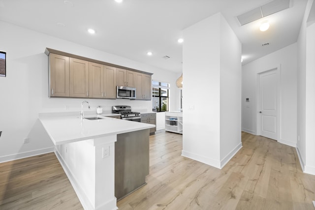 kitchen with sink, kitchen peninsula, a breakfast bar area, appliances with stainless steel finishes, and light wood-type flooring