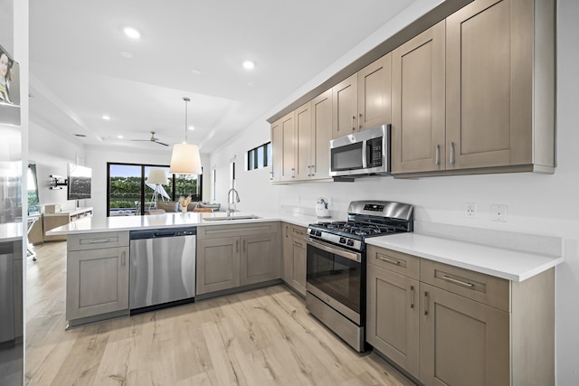 kitchen with kitchen peninsula, light wood-type flooring, stainless steel appliances, sink, and pendant lighting