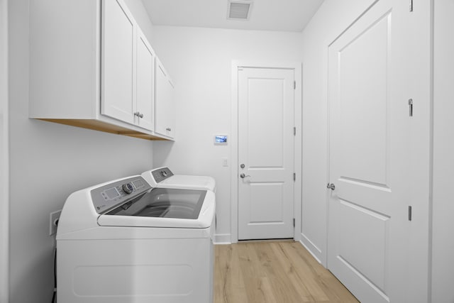 clothes washing area featuring cabinets, washing machine and dryer, and light hardwood / wood-style floors