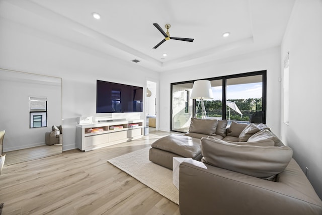 living room with light hardwood / wood-style flooring, ceiling fan, and a tray ceiling