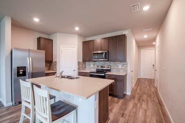 kitchen with appliances with stainless steel finishes, light wood-type flooring, dark brown cabinetry, sink, and a center island with sink