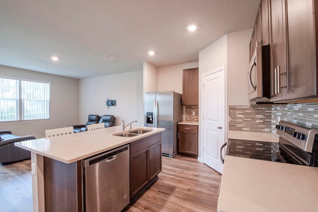 kitchen featuring light hardwood / wood-style flooring, sink, a center island with sink, tasteful backsplash, and stainless steel appliances