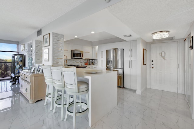 kitchen with white cabinets, appliances with stainless steel finishes, a textured ceiling, and a kitchen breakfast bar