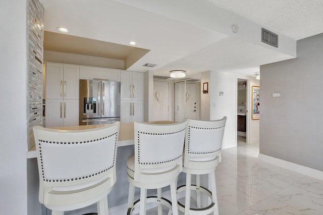 kitchen featuring stainless steel fridge, white cabinets, and a textured ceiling