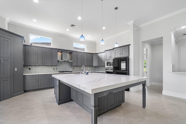 kitchen featuring a kitchen island with sink, wall chimney range hood, hanging light fixtures, ornamental molding, and stainless steel appliances