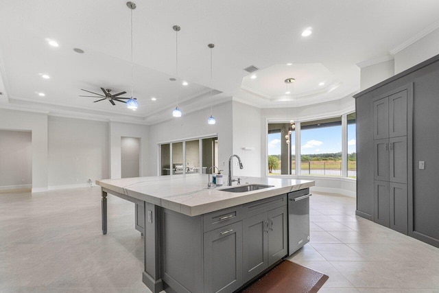 kitchen featuring gray cabinetry, sink, a raised ceiling, an island with sink, and pendant lighting