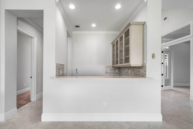 kitchen with decorative backsplash, ornamental molding, a textured ceiling, cream cabinetry, and light tile patterned flooring