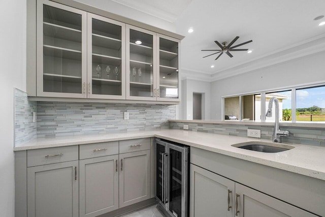 kitchen with sink, gray cabinets, light stone countertops, ornamental molding, and beverage cooler