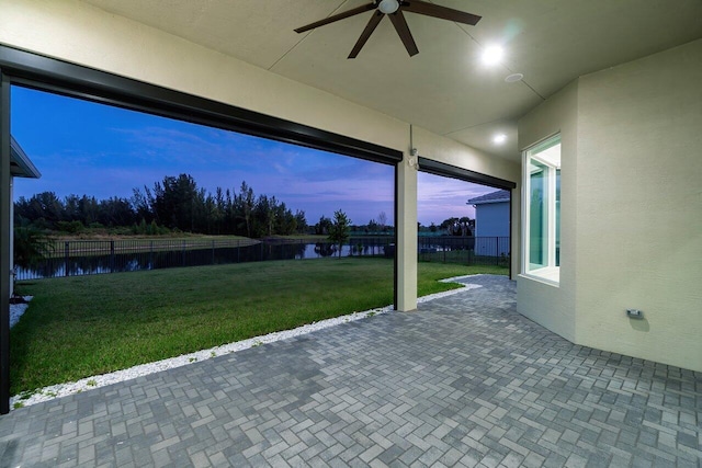 patio terrace at dusk featuring a yard, a water view, and ceiling fan