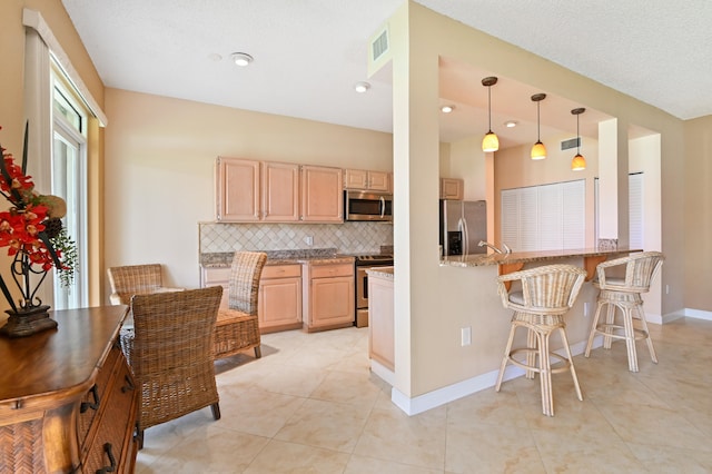 kitchen with light stone countertops, backsplash, kitchen peninsula, light brown cabinetry, and appliances with stainless steel finishes