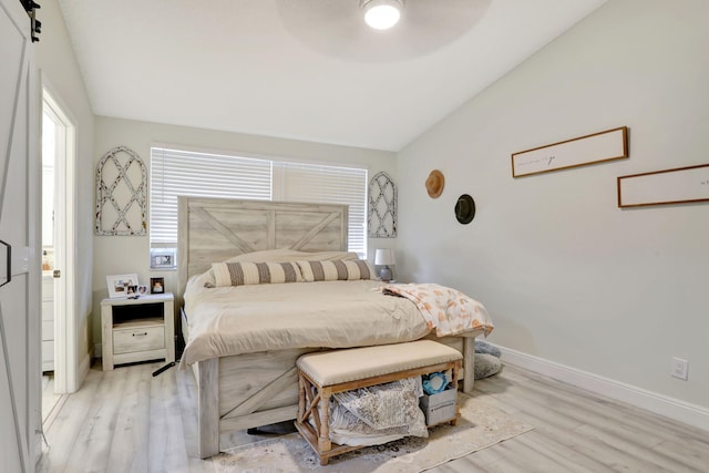 bedroom featuring ceiling fan, a barn door, lofted ceiling, and light hardwood / wood-style floors