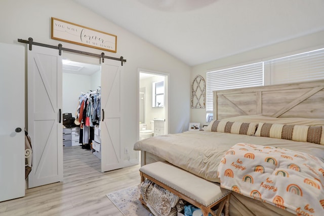 bedroom featuring a barn door, vaulted ceiling, light hardwood / wood-style floors, a spacious closet, and a closet