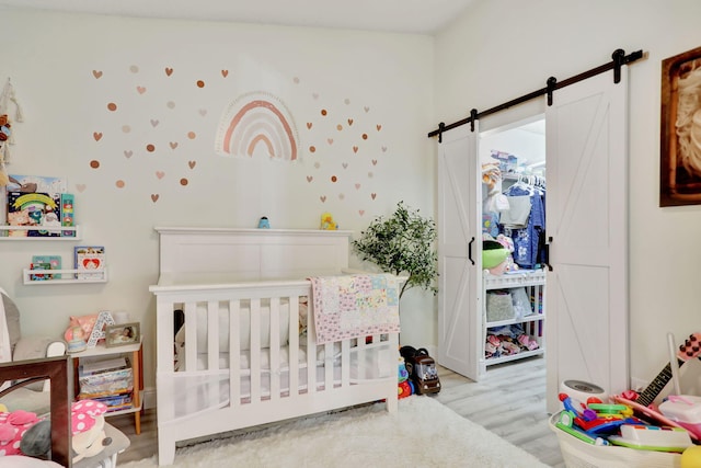 bedroom with light hardwood / wood-style floors, a nursery area, and a barn door