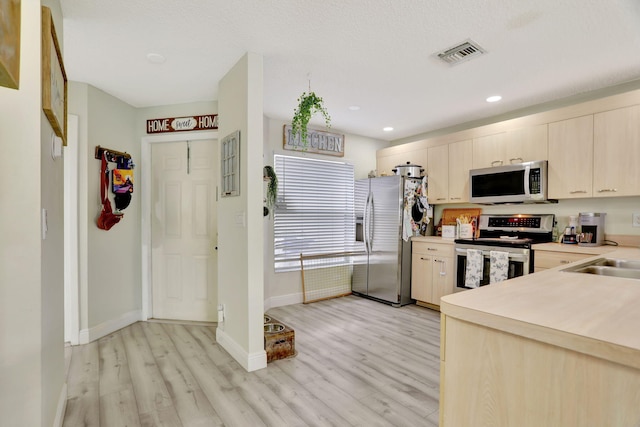 kitchen featuring stainless steel appliances, light brown cabinetry, light hardwood / wood-style floors, and sink