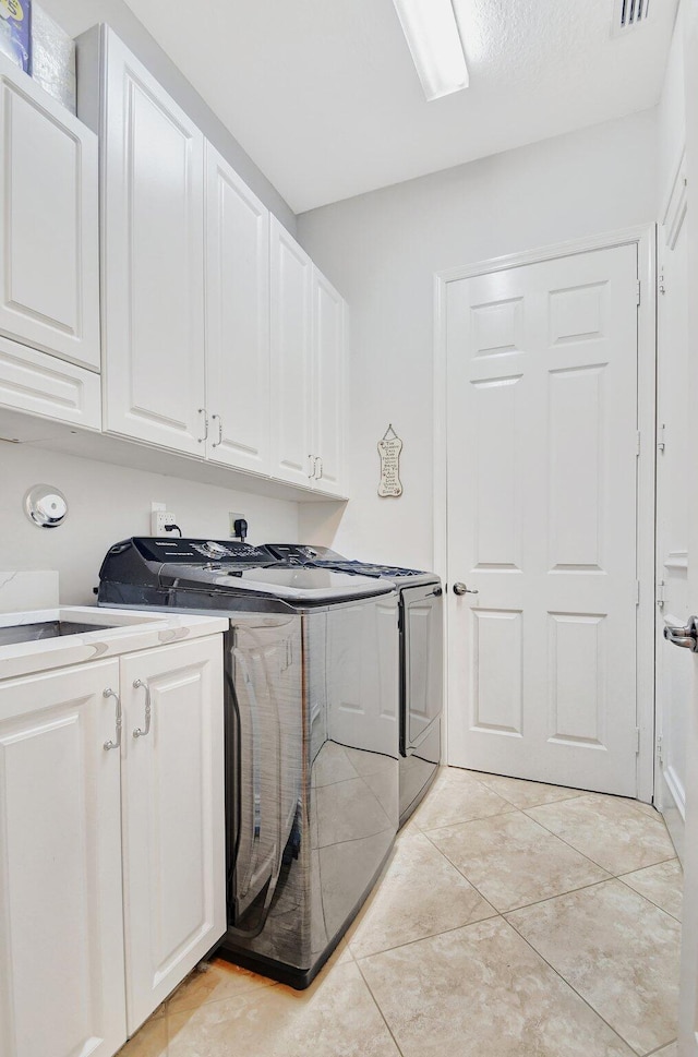 laundry area featuring light tile patterned flooring, cabinets, and washing machine and clothes dryer