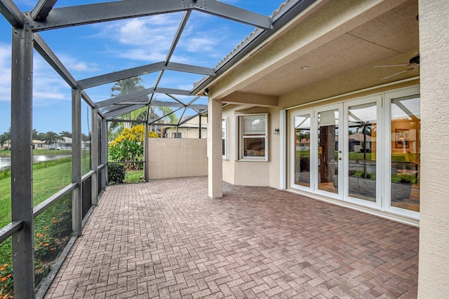 view of patio / terrace with french doors, a water view, glass enclosure, and ceiling fan