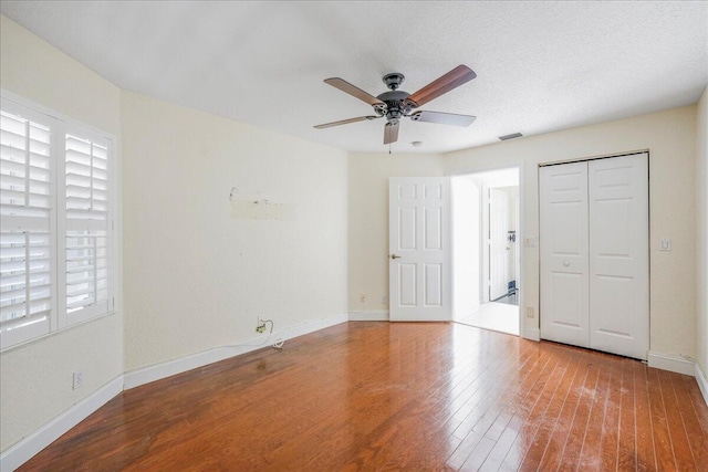 unfurnished bedroom featuring a closet, hardwood / wood-style flooring, multiple windows, and ceiling fan