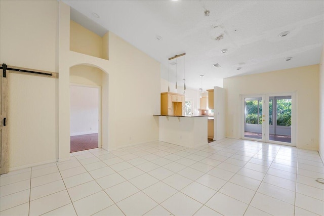 unfurnished living room with a barn door, light tile patterned flooring, and high vaulted ceiling