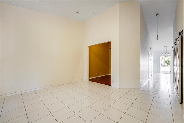 empty room with a barn door, light tile patterned flooring, and a high ceiling