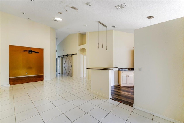 empty room with ceiling fan, a barn door, light hardwood / wood-style flooring, high vaulted ceiling, and a textured ceiling