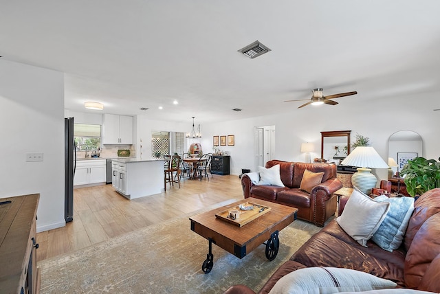 living room with ceiling fan with notable chandelier and light hardwood / wood-style floors